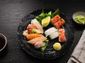Talerz z różnorodnym sushi: nigiri z łososiem, tuńczykiem, kalmarem, rolki z łososiem, awokado. Obok sos sojowy, wasabi i pałeczki. Czy sushi się podgrzewa? Nie, to danie serwuje się na zimno.