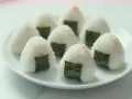 Kilka pysznych onigiri z łososiem, udekorowanych kawałkami nori, ułożonych na białym talerzu.