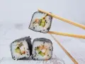 Rolka sushi z ogórkiem i rybą, podniesiona pałeczkami. Zastanawiasz się, ile octu ryżowego na 500g ryżu?