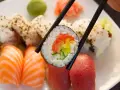 Pyszna rolka sushi z łososiem, ogórkiem i papryką, trzymana pałeczkami. Zastanawiasz się, ile waży rolka sushi?