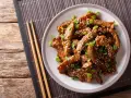 Pyszne kawałki wołowiny w sosie teriyaki, posypane sezamem i szczypiorkiem, gotowe do podania z pałeczkami.