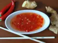 Ostry sos tao tao z kawałkami chili i imbirem, obok pałeczki i papryczki.