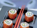 Cztery rolki sushi z awokado i rybą, obtoczone pomarańczową ikrą. Idealne sushi na diecie, podane z czerwonymi pałeczkami.