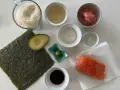 Wszystkie składniki do sushi: ryż, nori, łosoś, awokado, sos sojowy, wasabi, imbir marynowany, ocet ryżowy i sól.