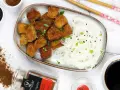 Chrupiące tofu w tempurze z makaronem ryżowym, posypane sezamem i szczypiorkiem. Obok sos sojowy i przyprawy.