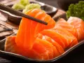 Sashimi co to? Świeży łosoś, chwytany pałeczkami, podany z wasabi i natką pietruszki.