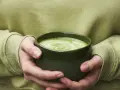 Dłonie trzymające zieloną miseczkę z pianką matcha.