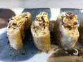 Trzy kawałki sushi z jajkiem, posypane czarnym sezamem i chrupiącymi dodatkami.