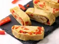 Roladki z jajek z papryką, przypominające omlet do sushi, ułożone na czarnej desce.