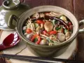 Gęsta zupa z grzybkami mun, enoki, pieczarkami, papryczkami chili i cebulką, podana w glinianym garnku.