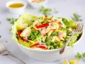 Kolorowa sałatka tajska z mango, papryką, cebulą i orzeszkami ziemnymi, podana w misce z sałatą.