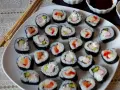 Talerz pełen sushi, w tym futomaki tamago z łososiem, awokado i paluszkami krabowymi.