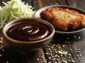 Gęsty, ciemny sos tonkatsu w miseczce, obok smażonego kotleta i poszatkowanej kapusty.