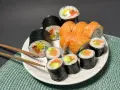 Talerz pełen sushi z łososiem i awokado. Wśród nich rolka z kremowym serkiem do sushi, idealna na przekąskę.
