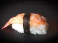 Nigiri ebi, czyli sushi z krewetką, na czarnym tle. Krewetka jest ułożona na ryżu, a całość spięta paskiem nori.