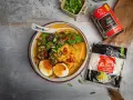 Aromatyczny ramen wołowy z tofu, jajkiem i grzybami shiitake. Obok opakowanie makaronu ramen.