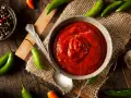 Miseczka z ostrym, czerwonym sosem, otoczona papryczkami chili, czosnkiem i pieprzem. Sriracha co to? To właśnie ten pikantny dodatek!