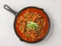 Kurczak w sosie gochujang, z zieloną cebulką i sezamem, podany na patelni.