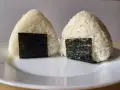 Dwa pyszne onigiri sushi, uformowane w trójkąty i ozdobione kawałkami nori, leżą na białym talerzu.