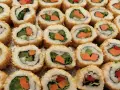 Roladki sushi z sezamem, w środku zielona sałata i pomarańczowa marchewka do sushi.