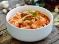 Aromaticzne curry z wieprzowiną w białej misce, ozdobione zieloną szczypiorkiem i czerwonymi papryczkami chili.
