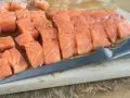Pokrojony w kostkę i plastry łosoś, idealny do sushi, leży na desce obok noża.