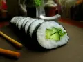 Świeży ogórek do sushi, zwinięty w rolkę z ryżem i nori. Obok leżą pałeczki.
