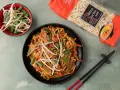 Pyszny makaron po azjatycku z kurczakiem, papryką i kiełkami fasoli mung. Obok opakowanie makaronu Chow Mein.