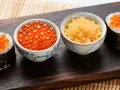 Dwa sushi rolki z pomarańczowym ikrą masago i miseczki z ikrą.