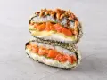 Sushiburger z łososiem, awokado i kremowym serkiem, otoczony chrupiącą panierką z ryżu i nori.