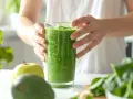 Zielony koktajl z awokado, kiwi i banana, gotowy do spożycia. Obok jabłko i świeży szpinak.