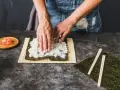 Dłonie rozprowadzają ryż na nori. Obok leżą pałeczki i marynowany imbir. To klucz do idealnego ryżu do sushi, który potrzebuje odrobiny octu.