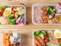 Cztery pudełka bento z kurczakiem, ryżem, warzywami i owocami. Idealne na zdrowy lunch, pokazują, bento co to jest.