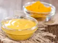 Dwie szklane miseczki na drewnianym tle. Jedna zawiera gładki sos, druga żółtą przyprawę, składniki do korma curry.
