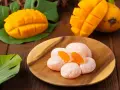 Słodkie mochi o smaku mango, ułożone na drewnianym talerzu, obok świeżych owoców i liści.