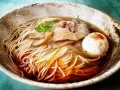 Miseczka aromatycznego ramenu z makaronem, jajkiem, mięsem i bambusem. Widać wyraźnie dodane ramen przyprawy, które nadają daniu głębi smaku.
