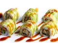 Sześć kawałków sushi dragon roll, udekorowanych plastrami awokado, sezamem i sosem.