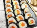Ułożone na czarnej desce rolki sushi z łososiem, tuńczykiem i warzywami. Obok pałeczki i bambusowa mata. Pyszne oshinko sushi!
