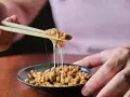 Pałeczki podnoszą lepką masę fasoli. To natto, co to jest? Japoński przysmak o charakterystycznym zapachu i smaku.