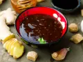 Sos teriyaki przepis: miseczka z ciemnym sosem, obok imbir, czosnek, cukier trzcinowy i miód. Idealny do dań azjatyckich.