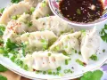 Pyszne pierożki gyoza posypane szczypiorkiem i sezamem, podane z aromatycznym sosem.