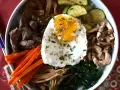 Apetyczne koreańskie dania: bibimbap z wołowiną, warzywami, grzybami i jajkiem sadzonym, posypane sezamem i szczypiorkiem.