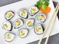 Talerz z hosomaki awokado, ogórkiem i marchewką, udekorowany wasabi i natką pietruszki.