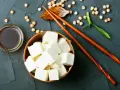 Kostki tofu, czyli przetworzona fasola sojowa, w drewnianej misce, obok sosu sojowego i pałeczek.
