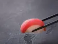 Pałeczki trzymają kawałek sushi z tuńczykiem. Czy sushi jest dobre? Wygląda apetycznie!