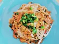 Pyszne tofu po chińsku z makaronem ryżowym, warzywami i szczypiorkiem na niebieskim talerzu.