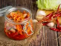 Słoik z kimchi na tle desek, z suszonymi papryczkami chili i czosnkiem.