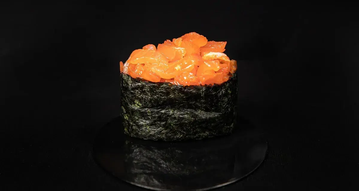Pyszny gunkan z tatarem z łososia, otoczony ciemną algą nori, prezentuje się apetycznie na czarnym talerzyku.