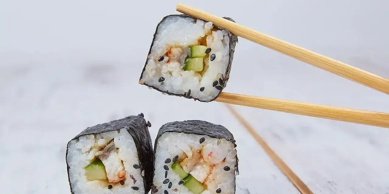 Rolka sushi z ogórkiem i rybą, podniesiona pałeczkami. Zastanawiasz się, ile octu ryżowego na 500g ryżu?
