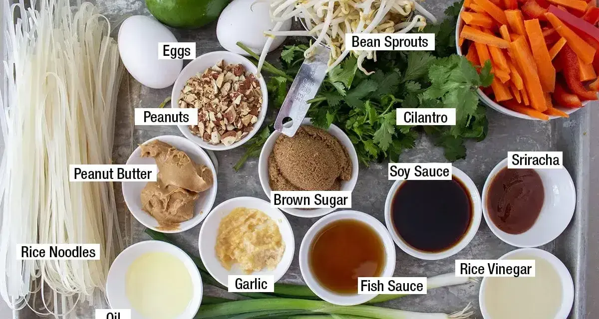 Składniki do sosu pad thai: makaron ryżowy, jajka, orzeszki ziemne, masło orzechowe, olej, czosnek, zielona cebulka, brązowy cukier, kiełki fasoli, kolendra, marchewka, papryka, sos sojowy, sos rybny, ocet ryżowy, sriracha, limonka.